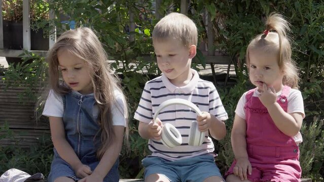 Portrait of Cute Little Three Children sitting on the beanch Garden. Cheerful Carefree Childhood. Preschool Siblings Friends Feeling Free Funky, Good Emotions Life. Home Dancing. Friendship Kids