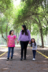 Single and divorced Latin mom and daughters walk in the park outdoors alone spend quality family time on summer vacation or weekend
