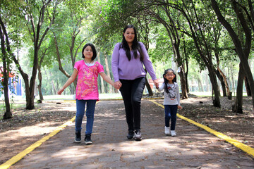Obraz premium Single and divorced Latin mom and daughters walk in the park outdoors alone spend quality family time on summer vacation or weekend 