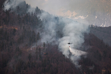 The helicopter carrying a bucket to deliver water for aerial firefighting in a mountain forest