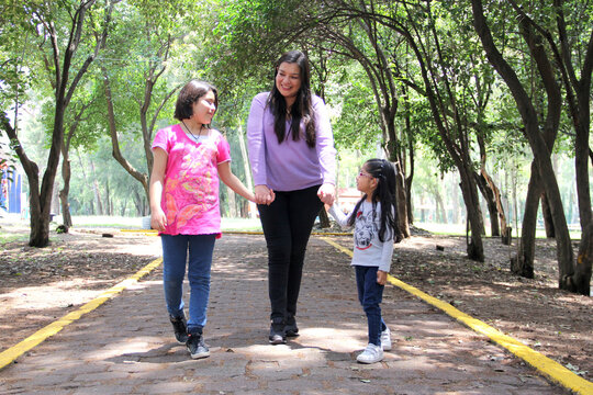 Single And Divorced Latin Mom And Daughters Walk In The Park Outdoors Alone Spend Quality Family Time On Summer Vacation Or Weekend
