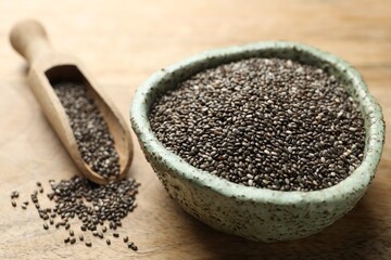 Bowl and scoop with chia seeds on wooden table, closeup