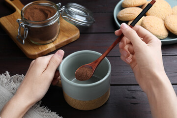 Woman pouring instant coffee into mug at wooden table, closeup