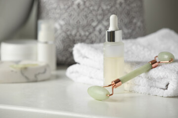Natural face roller, towels and serum on counter in bathroom. Space for text