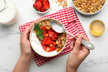 Woman eating tasty granola at white table, top view. Healthy meal