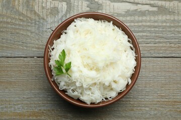 Tasty fermented cabbage with parsley on wooden table, top view
