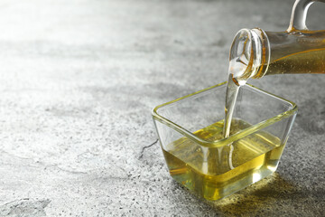 Pouring cooking oil from jug into bowl on grey table. Space for text