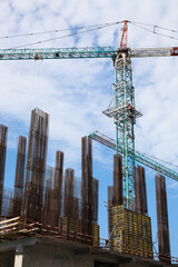 Naklejka premium Tower crane near building under construction against cloudy sky