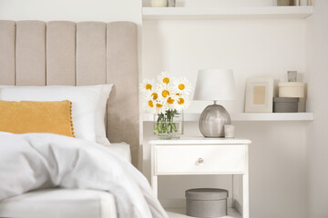 Bouquet of beautiful daisy flowers and lamp on nightstand in bedroom