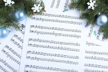 Fir branches, decorative snowflakes and light blue balls on Christmas music sheets, flat lay
