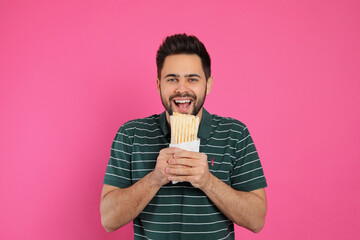 Young man eating tasty shawarma on pink background