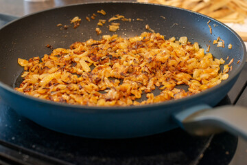A large black colored iron frying pan full of sweet white onions minced and chopped into being fried or sauteed in butter. The edges of the diced onion have browned and caramelized to sweeten. 