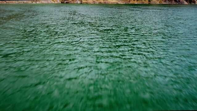 Aerial cinematic shot over turquoise green water revealing a mountain on Lake Quilotoa in Ecuador