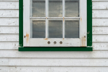 Obraz na płótnie Canvas A small single casement window in a white narrow wood beveled clapboard siding exterior wall of a vintage house. The glass window has six panes with green decorative trim on the outside edge. 