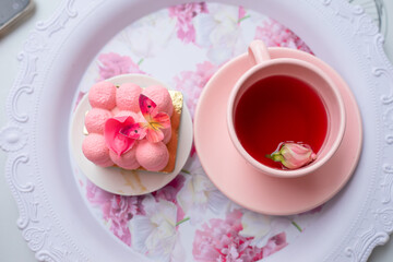 Sugar sweet pink cube ball velours mousse cake dessert with butterfly decoration on plate and cup of tea with rose bud