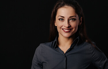 Fototapeta premium Beautiful thinking toothy smiling business woman in blue shirt on black background with empty copy space for text. Closeup