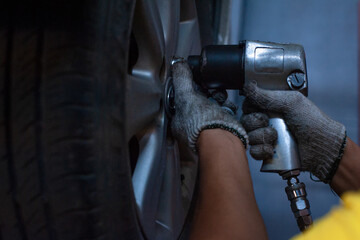 Hands of mechanic changing car wheel in auto repair service with Impact Wrench - 525448377