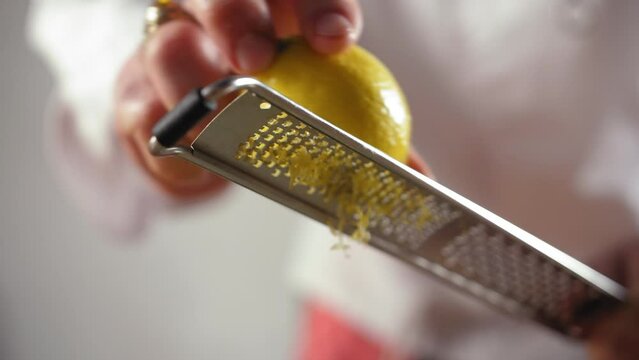 Close Up Shot of a Professional Chef Grating Lemon on a dish, slow motion shot, blurred white background