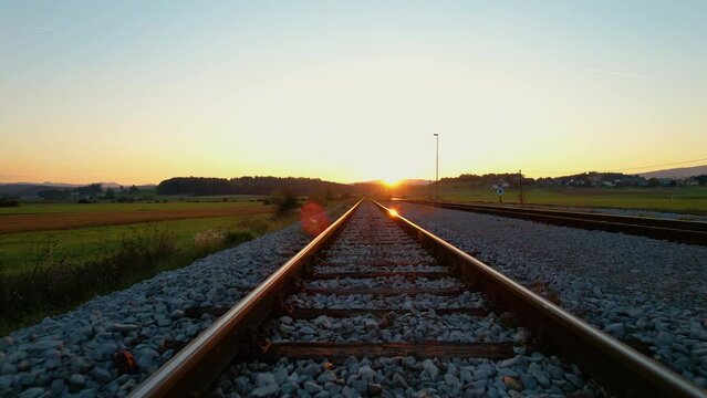 LOW ANGLE: Movement along orange glowing railroad tracks in golden autumn light. Countryside railway passing beautiful hilly landscape. Detailed view of railway tracks and beams for train transport.