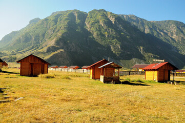 Several small wooden houses in a picturesque valley surrounded by mountains on an early autumn morning.