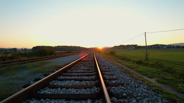 LOW ANGLE: Moving above glowing golden lit railroad tracks in autumn morning. Countryside railway passing gorgeous hilly landscape. Overview of railway tracks and junction near train station.