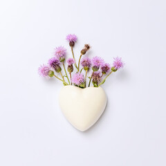 Small burdock flowers in a white magnetic pot on white background
