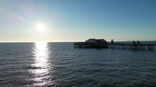 Aerial drone flight heading out to sea heading over a pier at Blackpool Beach with the sun shining down over the ocean