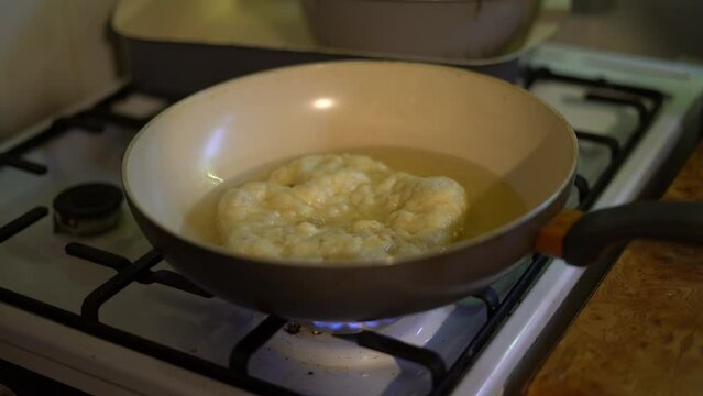 Checking if Hungarian food Langos is done frying in pan with tongs, home kitchen