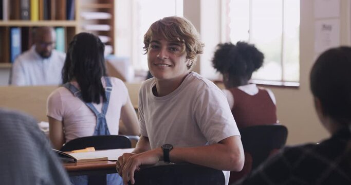 Happy boy high school student learning in a classroom getting an education, development and knowledge. Smart, diversity and creative students with male teenager sitting in desk tables and studying