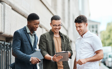 Casual group of IT engineers preparing for a meeting on a digital tablet outside together. Diverse team of happy technicians talking and reading plans and strategy for a startup or project