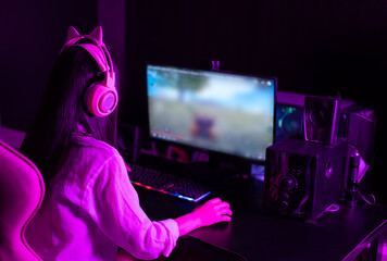 Asian woman wearing headphones playing a first-person shooter online video game on her computer.