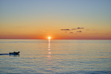 Sunset over the sea with a sailing boat in the distance.