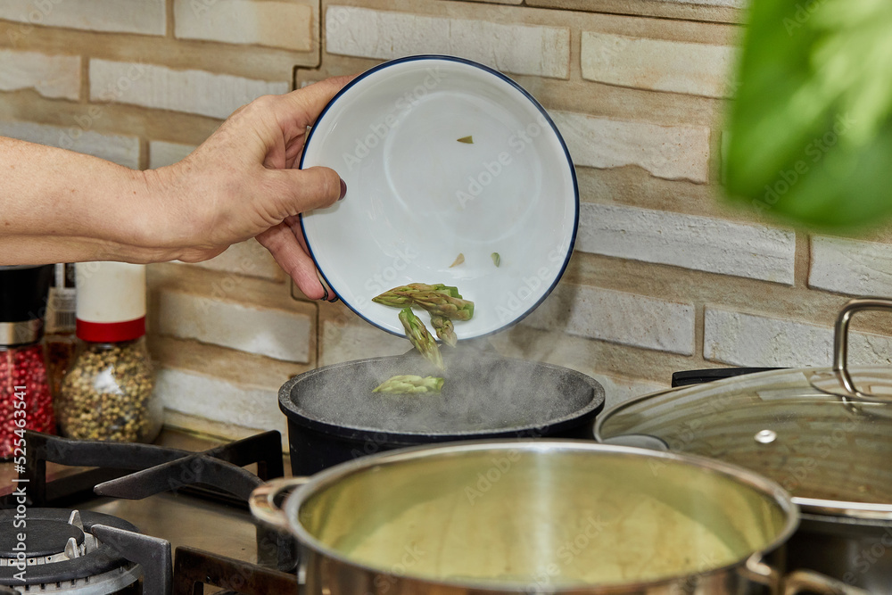 Sticker Chef throws asparagus heads into a pot on a gas stove