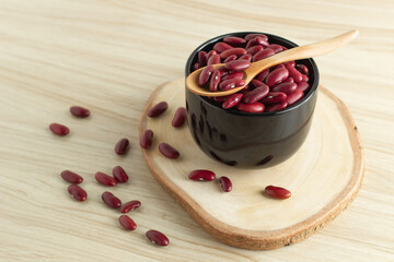 red kidney beans in a black bowl and spoon on wooden background, front view, selective focus.