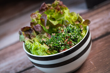 Parsley salad or Tabbouleh, easy and healthy classic vegetarian dish with bulgur, tomatoes, parsley, spring onion and mint, olive oil on dark wooden background, High quality photo