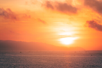 Naklejka na ściany i meble Beautiful cloudscape over the sea, sunrise shot. Lonely boats. Vung Tau beach, Vietnam with beautiful yellow sunrise sky, sun and clouds in orange and blue tones.