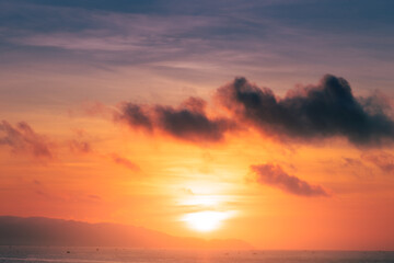 Naklejka na ściany i meble Beautiful cloudscape over the sea, sunrise shot. Lonely boats. Vung Tau beach, Vietnam with beautiful yellow sunrise sky, sun and clouds in orange and blue tones.