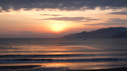 Peaceful morning landscape with sunrise at the sea shore with little fishing boat and  mountains in the distance. Summer vacation near the sea  or traveling concept