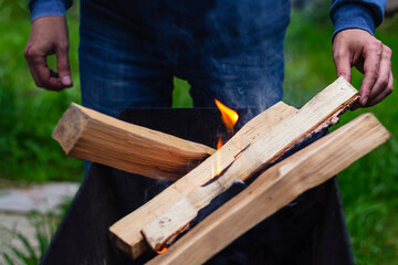 Backyard picnic. Man throws firewood into brazier. Preparing for picnic. Camping lifestyle.