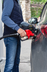 Man's hand holds a red fuel pump for refueling, refueling his black car at gas station.