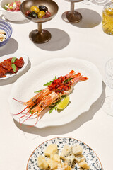 Seafood appetizer - baked langoustines with tomato tartar on white table. Grilled shrimp in italian restaurant menu. Langoustines on white background with shadows. Shrimp appetizer. Baked prawn.