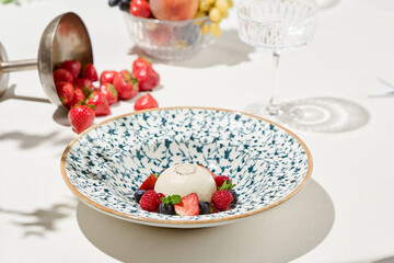 Classic panna cotta with berries on light background. Italian dessert from milk jelly - panna cotta. Desserts menu. Aesthetic composition with panna cotta and strawberries, raspberry and blueberry.