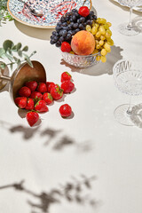 Summer background with fruits, berries and wine glass on white table. Light background with shadows from wine glasses and fruit with copy space. Summer food backdrop with empty place. Summer menu.