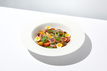 Traditional french salad nicoise with tuna, potatoes, eggs and vegetables on white table with harsh shadows. Tuna salad with quail eggs on white background with shadows of leaves.