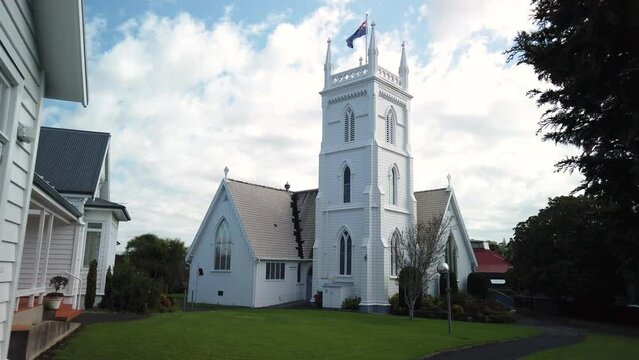 Approach to white old wooden historic church building with New Zealand flag in Auckland city.