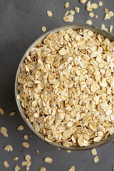 Dry Organic Rolled Oats in a Bowl on a gray surface, top view. Flat lay, overhead, from above.