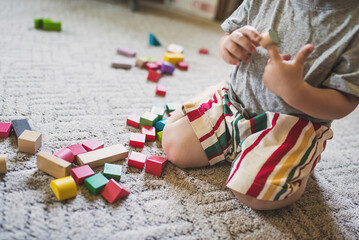 A little boy, 2 years old, sits on the floor and carpet at home and plays with colored wooden blocks. Educational toy constructor. The child learns to play according to the Montessori method