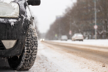 Black car with studded wheels parked by the side of the road on a cold winter day