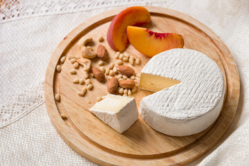Delicious young homemade Camembert cheese on a wooden board with peach nuts and slices. Selective focus on a piece of cheese