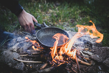 a man with a frying pan over a campfire, cooking while camping